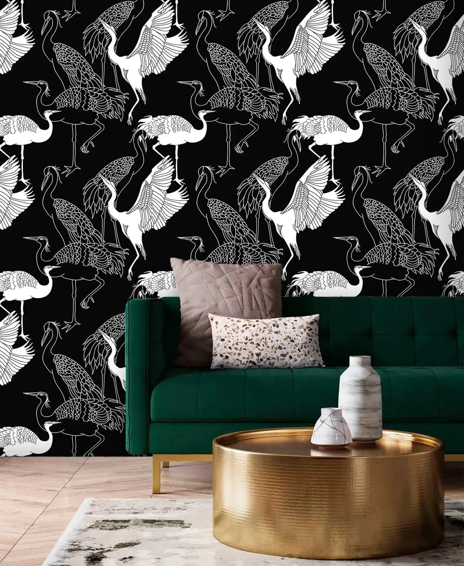 Monochrome crane wallpaper with white line-drawn cranes on black behind an emerald velvet sofa and gold table