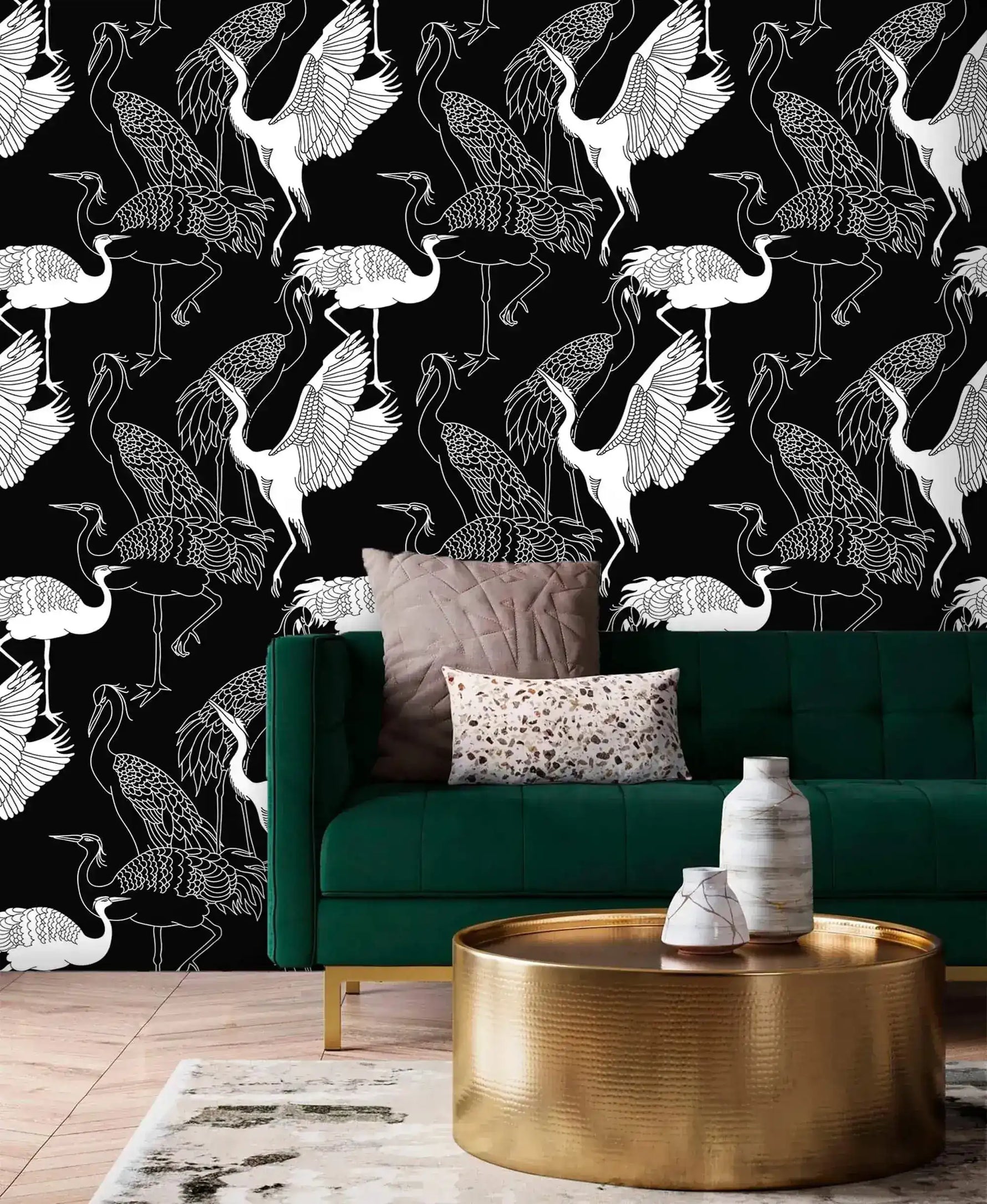 Monochrome crane wallpaper with white line-drawn cranes on black behind an emerald velvet sofa and gold table