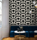 Monochrome deco fan wallpaper above a blue velvet banquette with marble bistro tables in a lounge