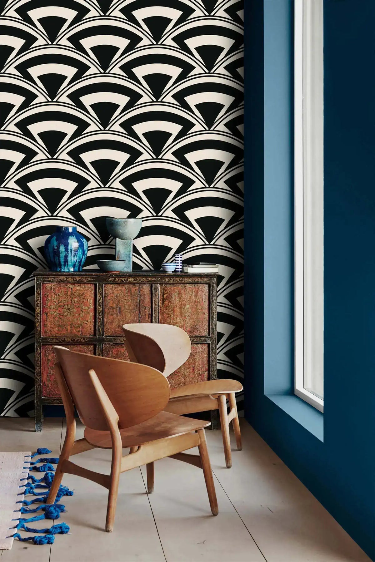 Monochrome deco fan wallpaper beside a blue wall with antique cabinet and curved wood chairs