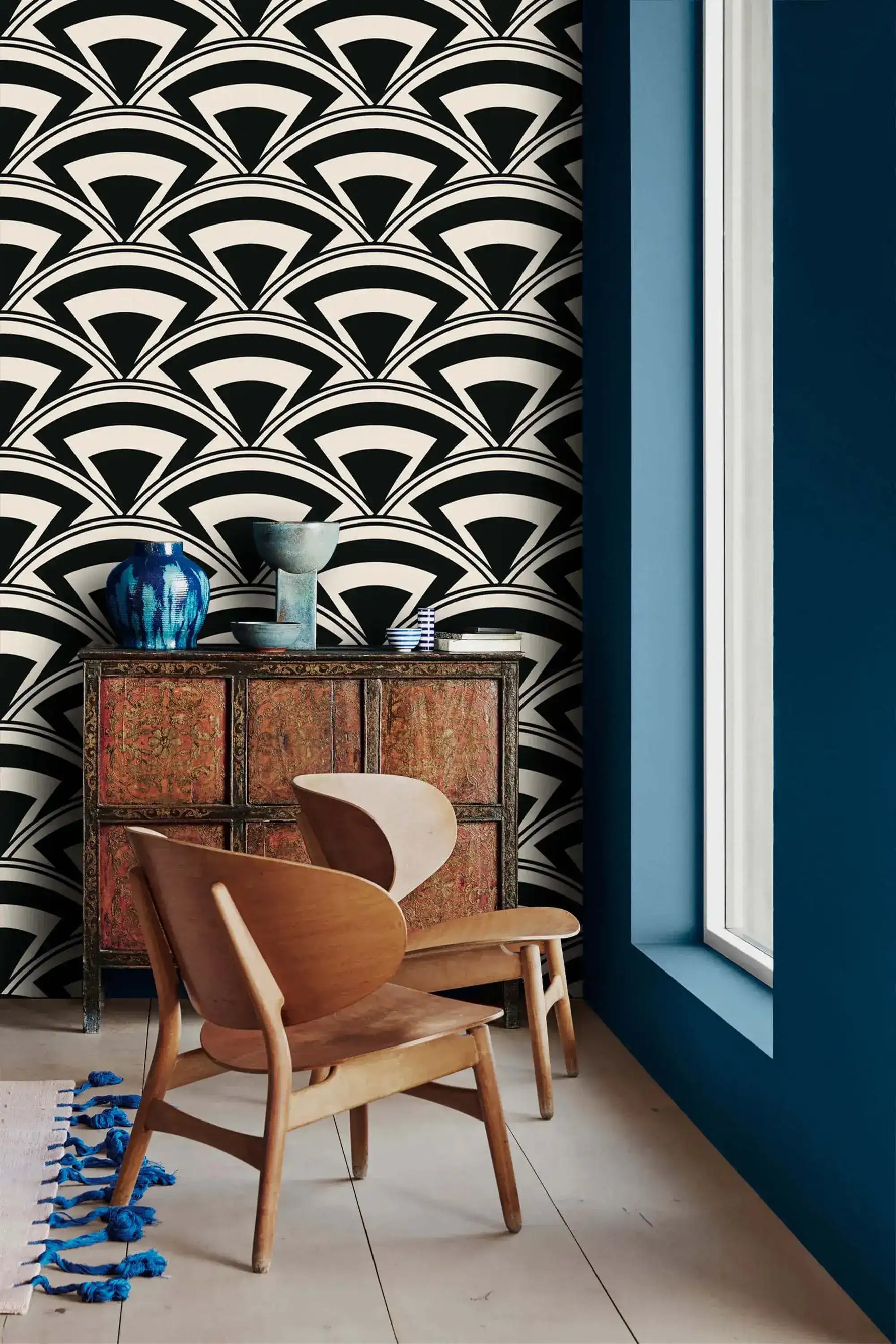 Monochrome deco fan wallpaper beside a blue wall with antique cabinet and curved wood chairs