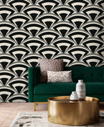 Monochrome deco fan wallpaper in black and cream behind an emerald sofa with brass drum table