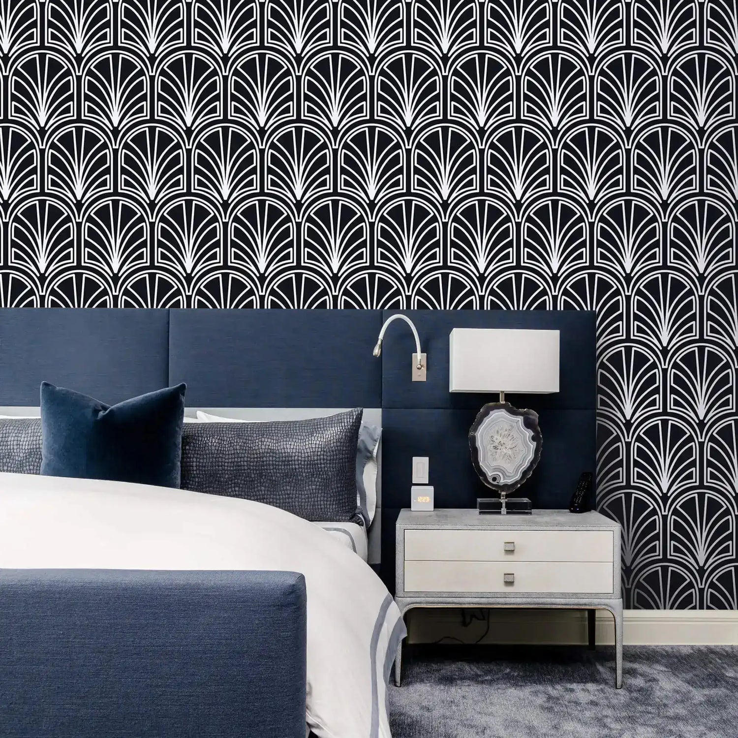 Monochrome vintage geometric wallpaper, white art deco palmette fans on navy behind an upholstered bed