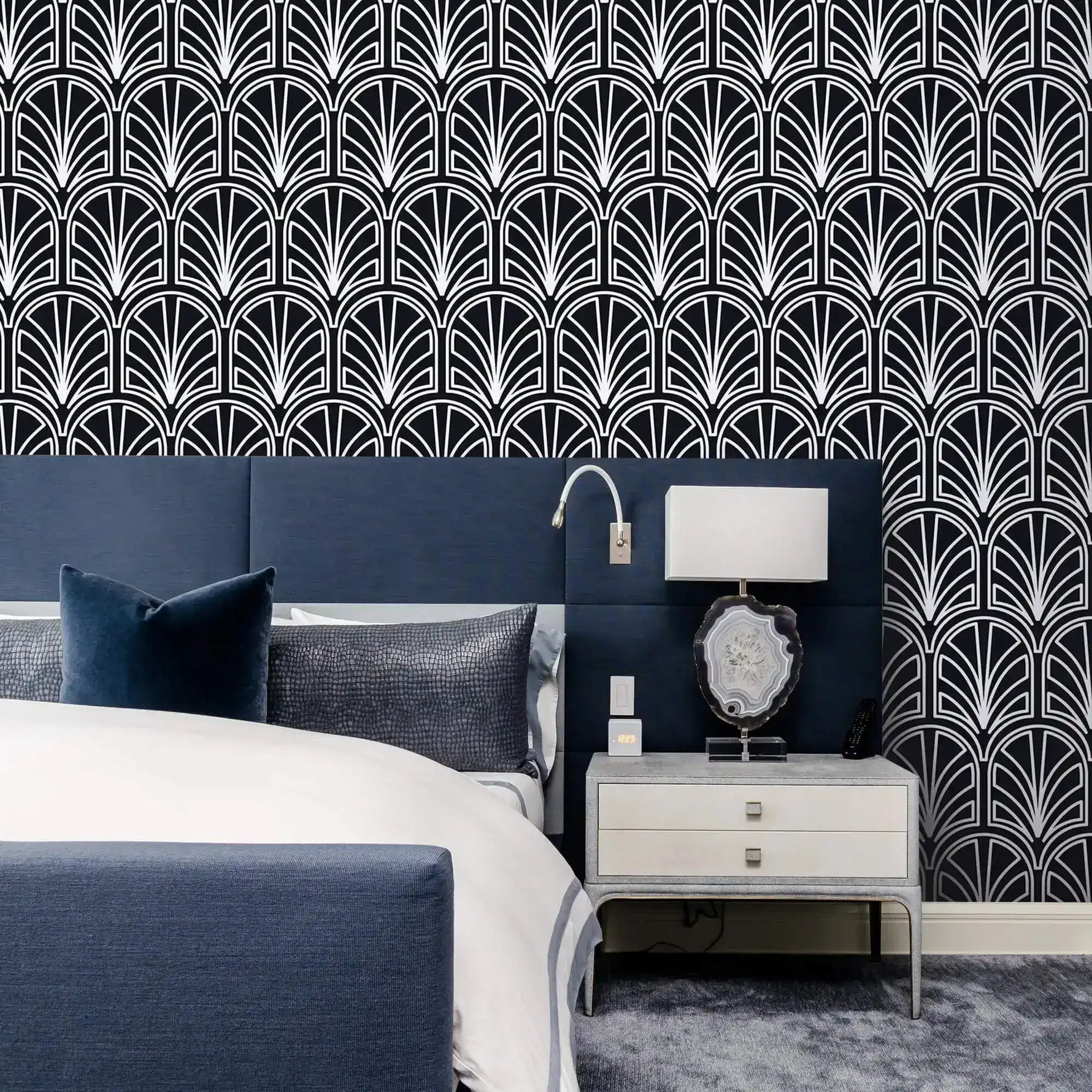 Monochrome vintage geometric wallpaper, white art deco palmette fans on navy behind an upholstered bed