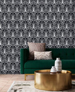 Monochrome vintage geometric wallpaper, white deco palmettes on black behind an emerald velvet sofa