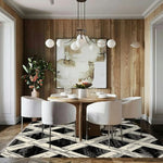 Elegant dining room featuring a Monochrome Weave Hand Tufted Area Rug under a round wooden table with white chairs. The large area rug has a geometric pattern in black and white, ideal for adding a modern touch to bedrooms or living spaces. A wool rug that complements the wood-paneled walls and abstract artwork, creating a cozy and stylish atmosphere.