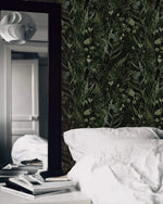 Moody fern botanical wallpaper behind white bedding with tall floor mirror and stacked books