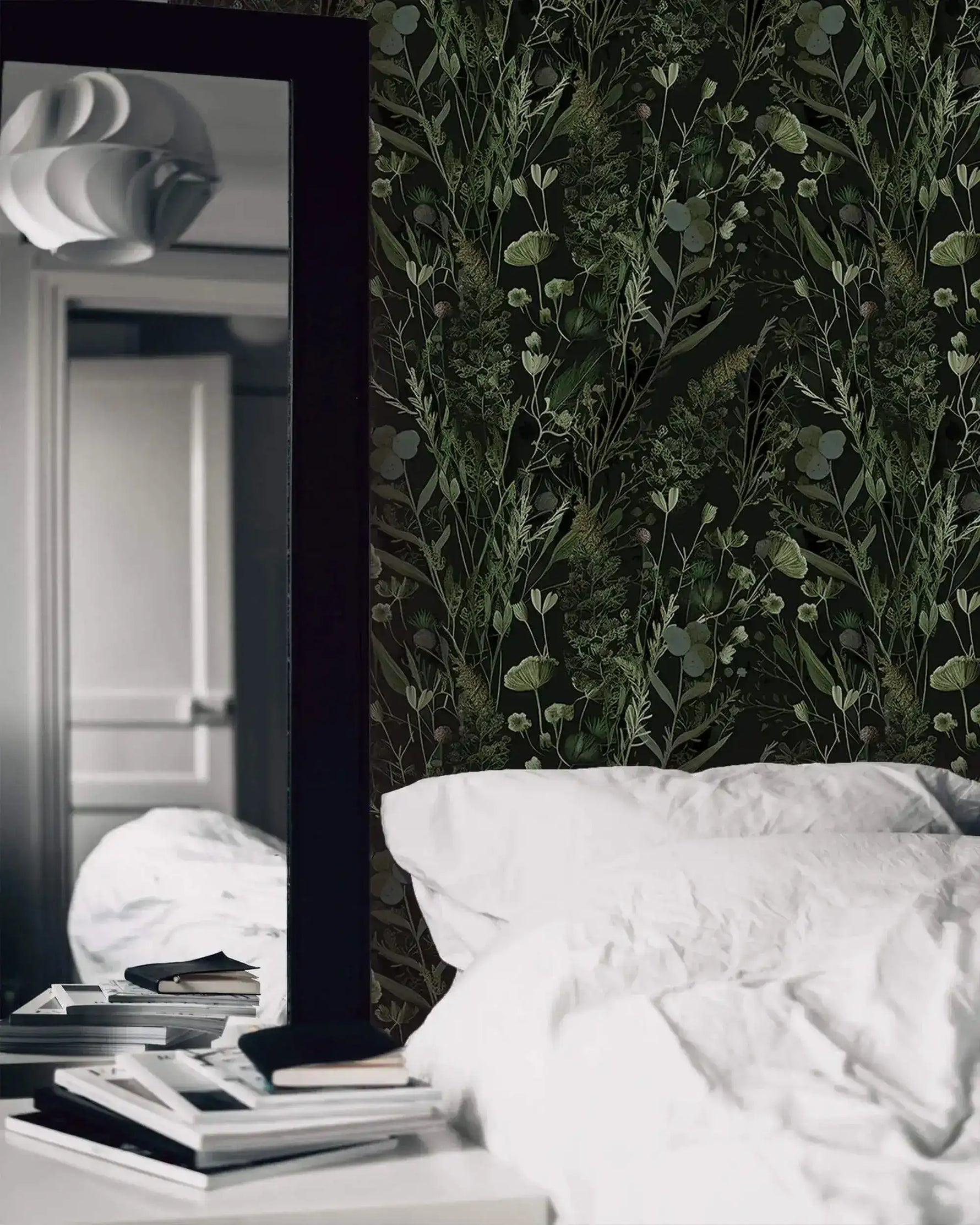 Moody fern botanical wallpaper behind white bedding with tall floor mirror and stacked books