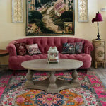 A vibrant multicolored floral wool hand-knotted area rug under a round wooden coffee table in a cozy living room setting. The square rug features intricate Persian-inspired designs, making it an ideal dining table rug or dining room carpet. The rich, colorful patterns of this floral rug add warmth and elegance to the wool rug, complementing the plush pink sofa and decorative pillows.
