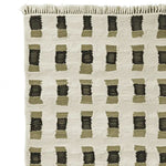 Close-up view of a contemporary hand-knotted wool rug with a geometric pattern, perfect for enhancing living room area rugs. The design features a grid of black and olive rectangles on a neutral background, showcasing modern elegance in area rugs.