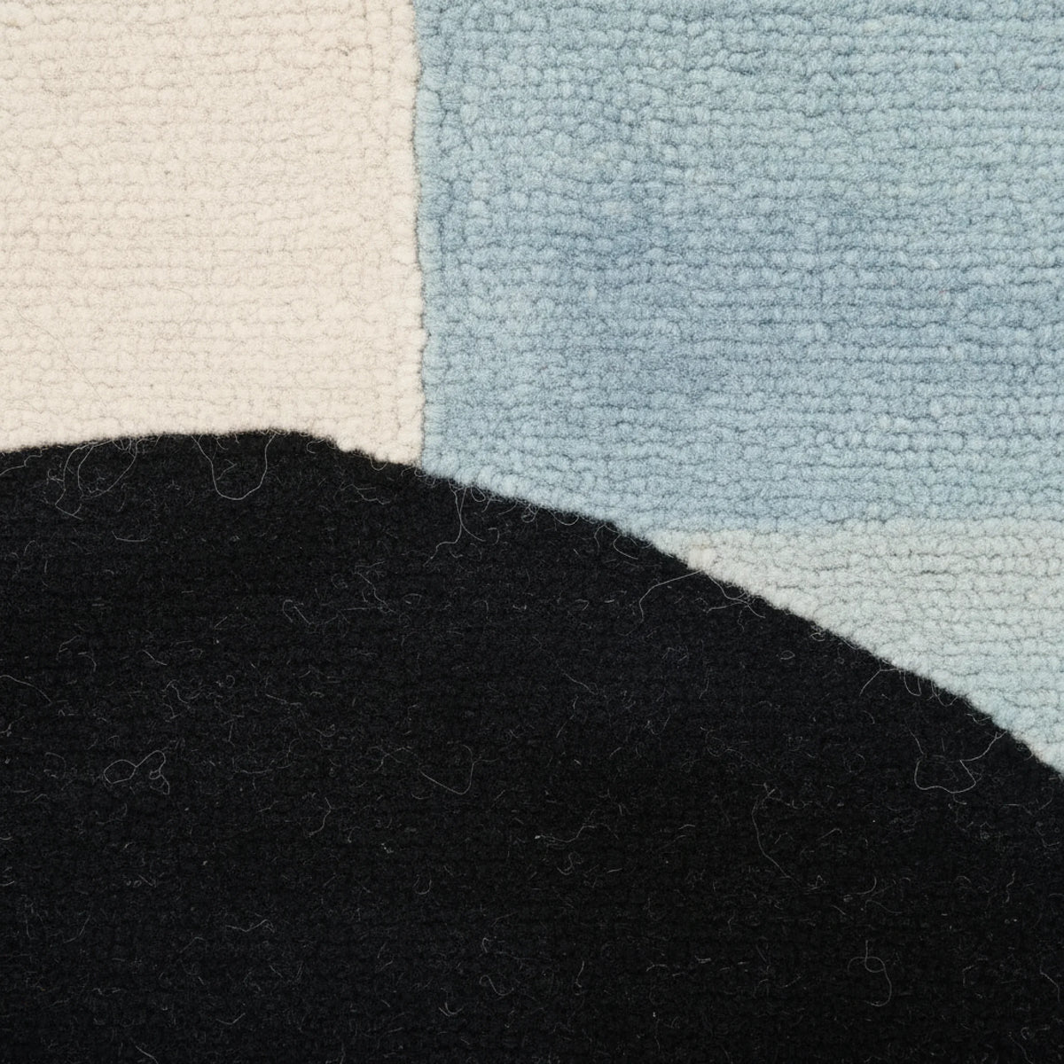 Close-up of a textured rug with black, beige, and blue sections.