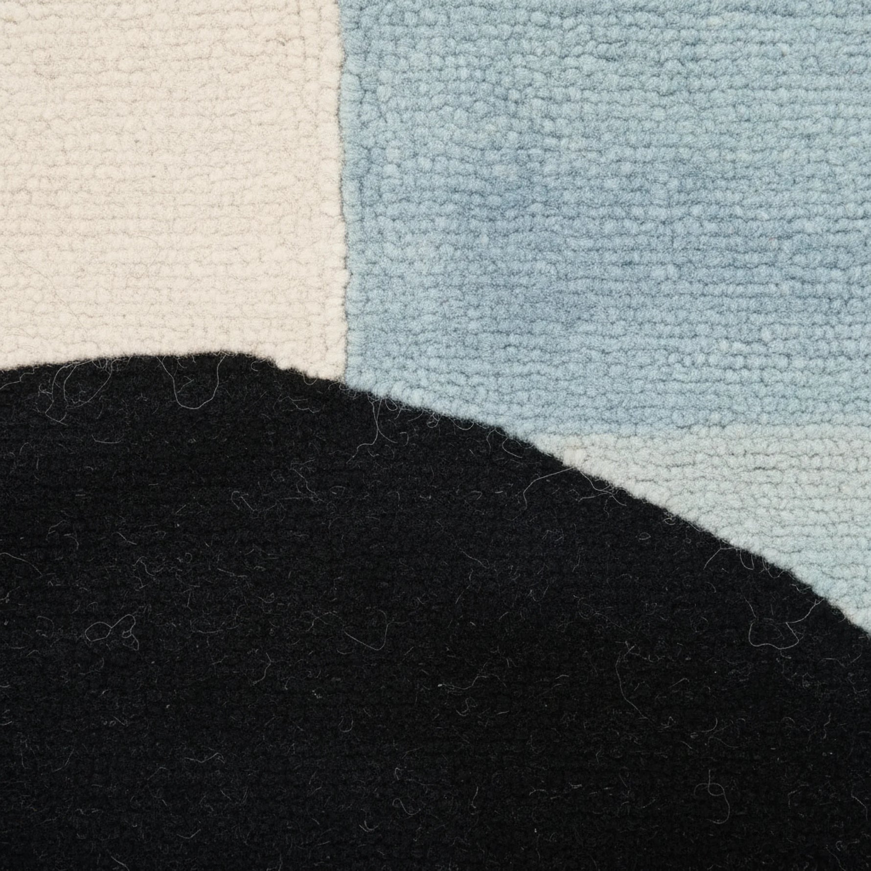 Close-up of a textured rug with black, beige, and blue sections.