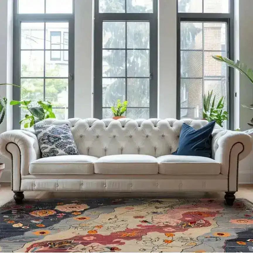 A chic living room featuring a Mystic Meadow Hand Knotted Area Rug with vibrant abstract patterns. This contemporary wool rug adds warmth and style to the space, complementing the elegant white sofa and large windows. Ideal for living rooms and offices, this square area rug enhances any modern decor.