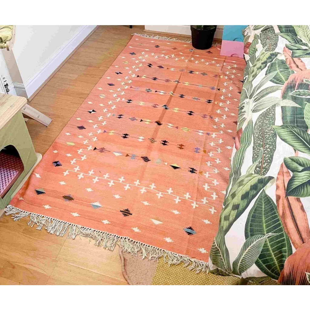 A beautifully designed Natural Vegetable Dyed Indian Dhurrie Reversible Cotton Rug in Blush Galaxy, laid out in a cozy living room setting. The area rug features intricate patterns in a boho style with soft hues, making it an ideal choice for living room area rugs. Perfect for those looking for stylish and sustainable cotton rugs to enhance their living space.