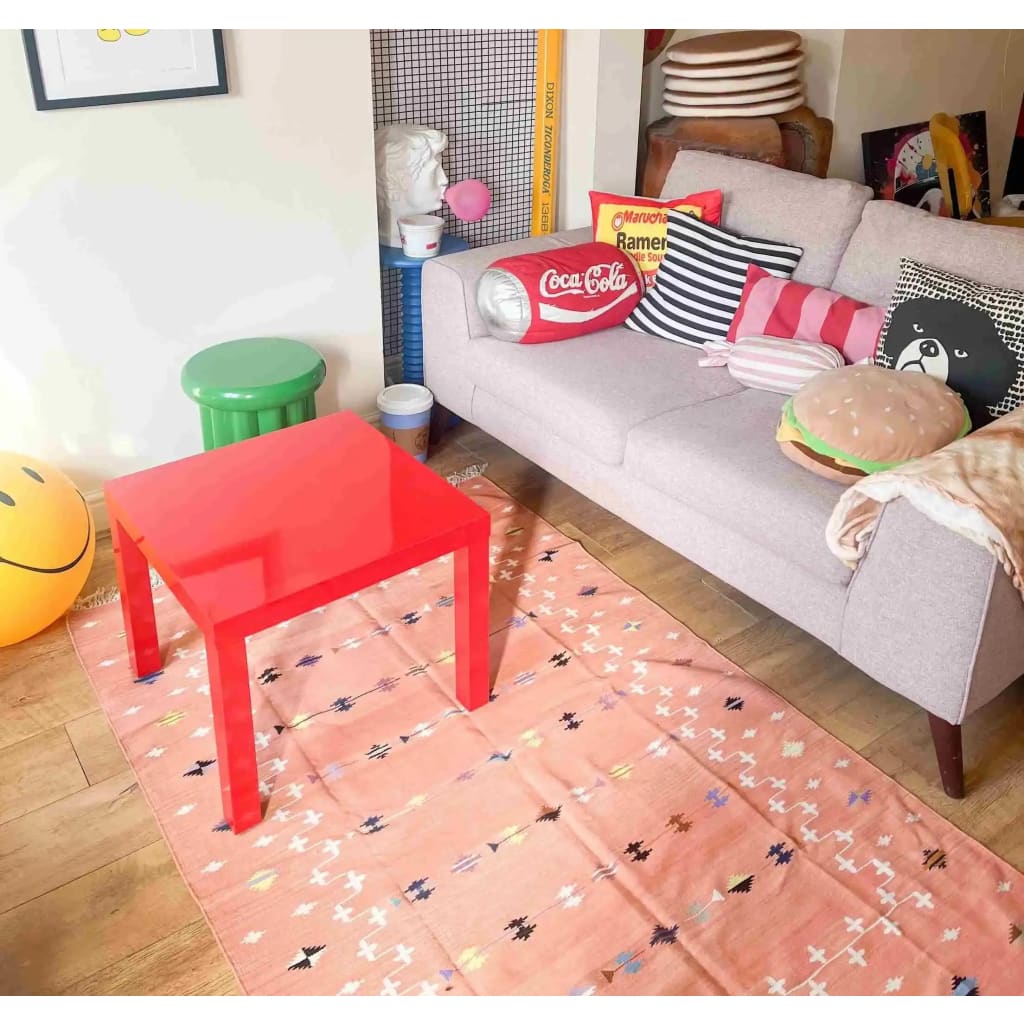 A cozy living room featuring a blush galaxy cotton area rug with boho patterns. The rug complements the eclectic decor with a vibrant red table and a sofa adorned with colorful pillows. Perfect for those seeking stylish rugs for living room or boho-inspired living room area rugs.