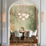 A sophisticated living room featuring a Nature's Elegance Hand Knotted Area Rug with intricate floral patterns. This Persian-style rug enhances the elegant dining setup with soft grey chairs and a round wooden table, framed by a serene nature-themed wall mural. Ideal for those seeking luxurious area rugs for living rooms.