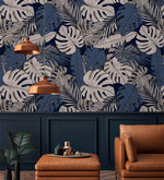 Navy tropical midnight leaves wallpaper above paneled wainscoting, styled with leather armchair and copper pendants