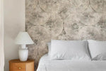 Close-up of beige concentric-circle geometric wallpaper beside a bed with a white lamp and oak nightstand