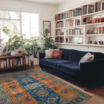 A vibrant and cozy living room featuring a Nomadic Heritage Knotted Wool Rug. The area rug, with its vintage design, adds a splash of color to the room, complementing the blue sofa and surrounding greenery. Ideal for living room and dining room spaces, this wool rug enhances the warmth and style of the home.