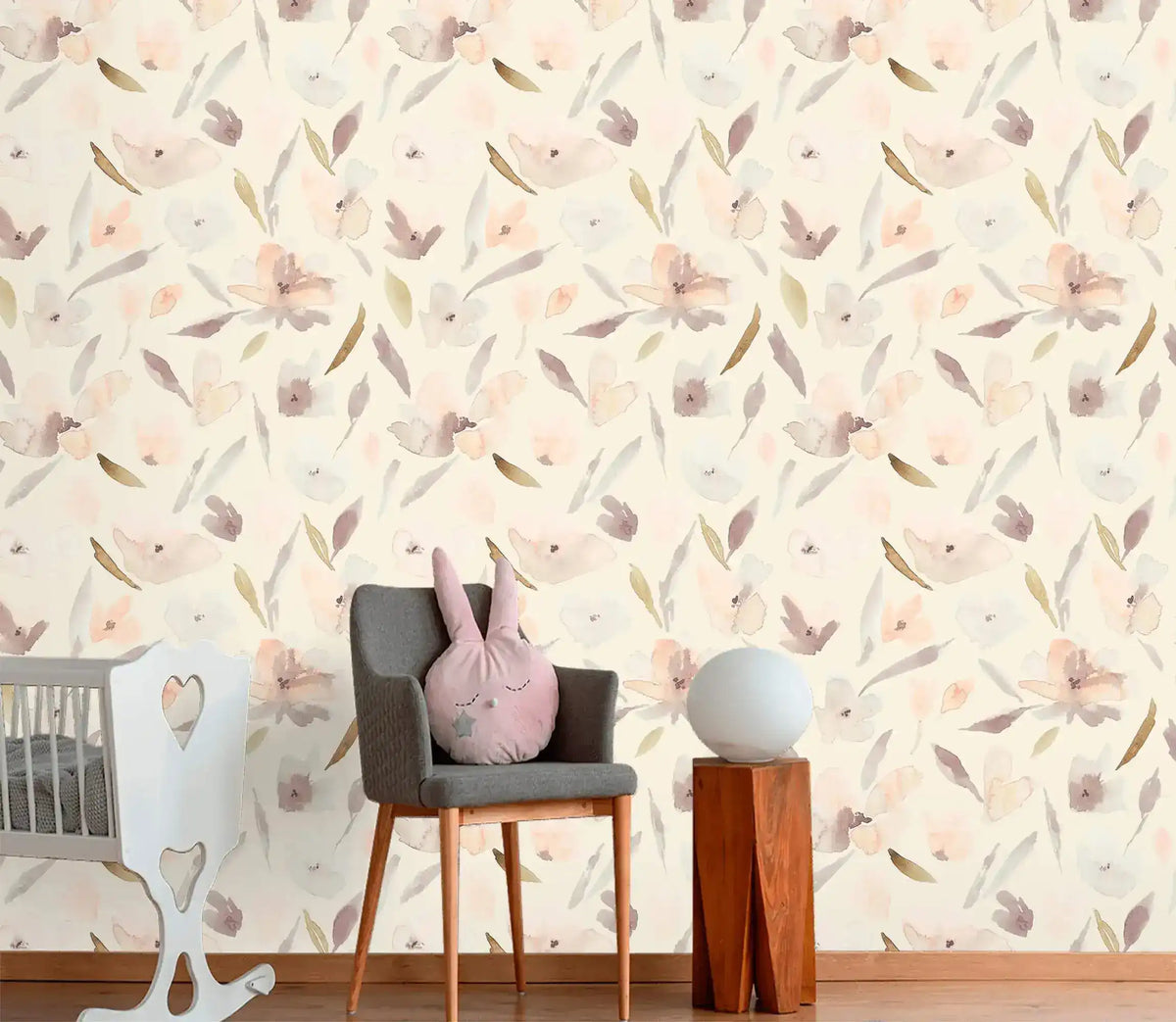 Nursery with grey chair and crib against pastel watercolor blossom wallpaper on cream