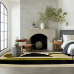 A contemporary area rug with an abstract design featuring earthy tones of black, green, and beige, placed in a modern dining room setting. The wool rug complements the minimalist decor, with a stylish chair and side table near a sleek fireplace, making it perfect for formal dining rooms and living room spaces.