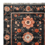Close-up of the Obsidian Floral Frame Hand Knotted Area Rug, showcasing intricate floral patterns in warm hues on a dark backdrop. This wool rug is perfect as a living room rug measuring 8x10, adding elegance and style.