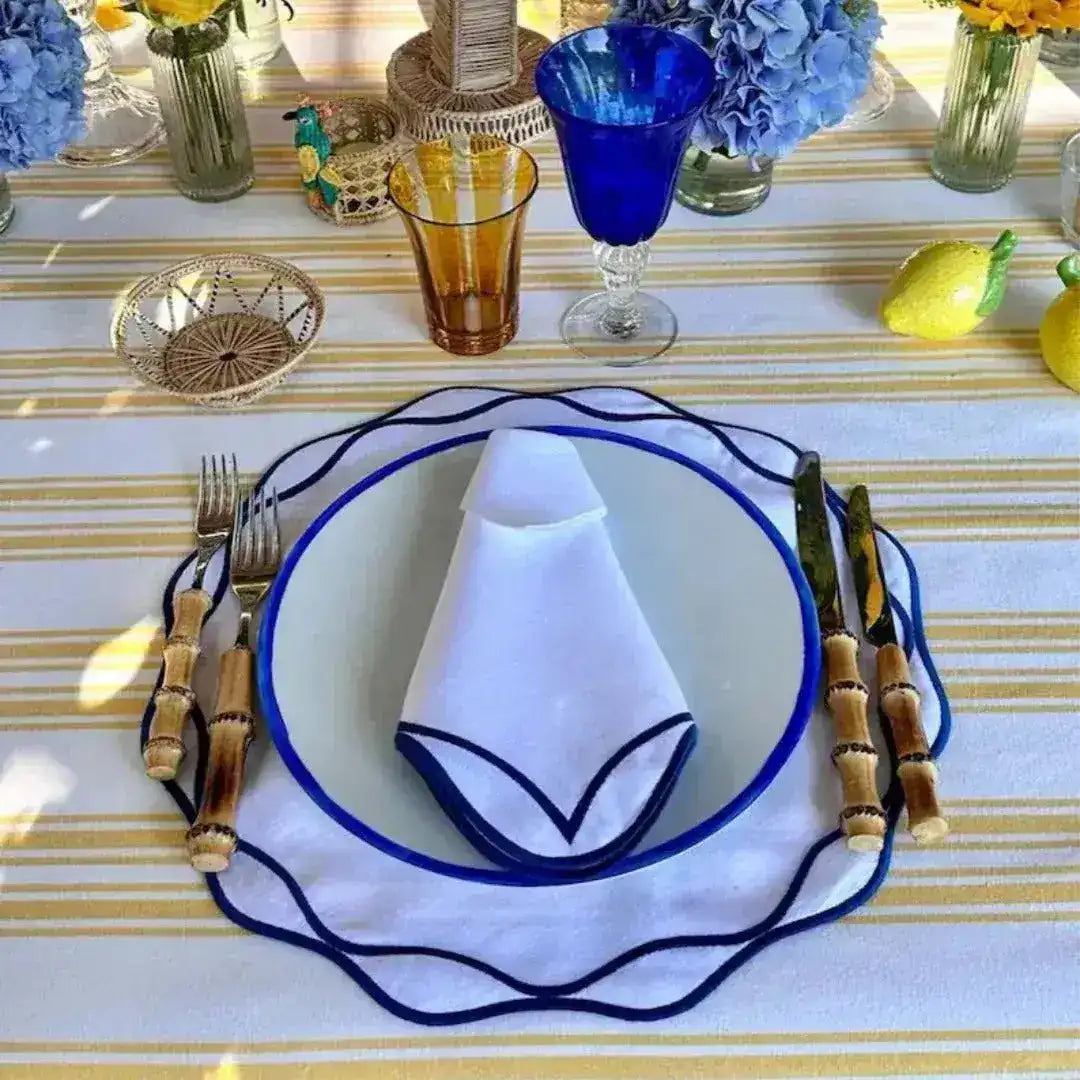 White ocean ripple placemat with navy scalloped wavy border, blue-rimmed plate, bamboo cutlery, blue hydrangeas