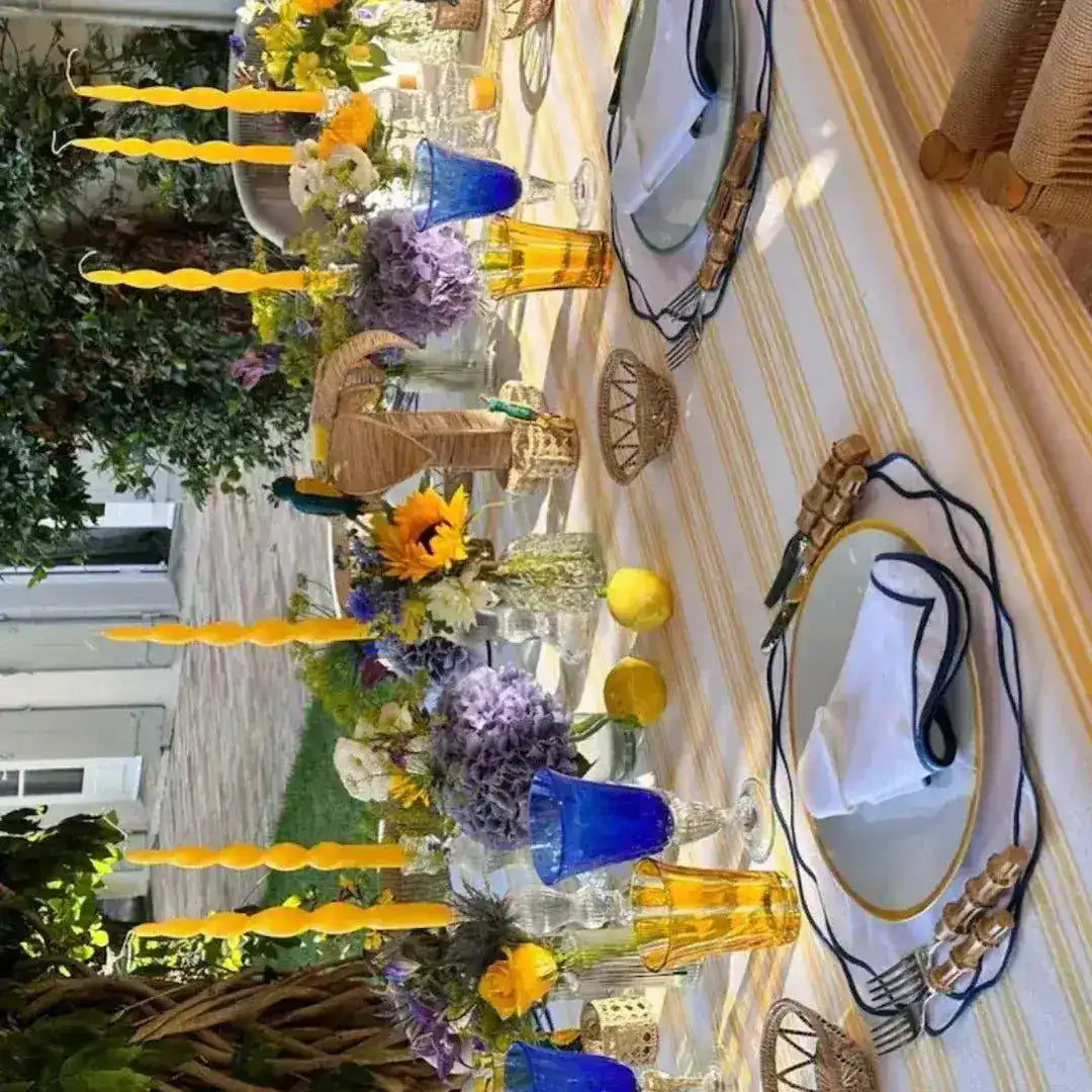 Wide outdoor table with ocean ripple placemats, navy wavy borders, yellow candles, purple florals and lemons