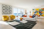 Modern living room with green rug, yellow chairs, white sofa, and colorful artwork.