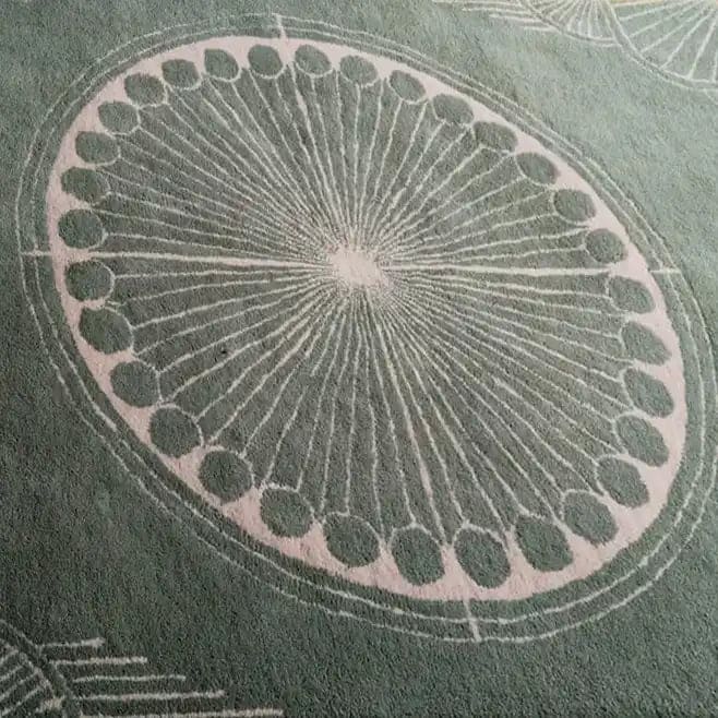 This image showcases a close-up of an Olive Green Moon Art Deco Hand Tufted Wool Rug, featuring an intricate circular pattern in soft tones. Perfect for adding a touch of elegance to your living room or office, this area rug combines style and comfort, making it an ideal choice for those seeking premium wool rugs for their space.