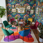 Colorful dining room with a round table and multicolored chairs against a floral wall.