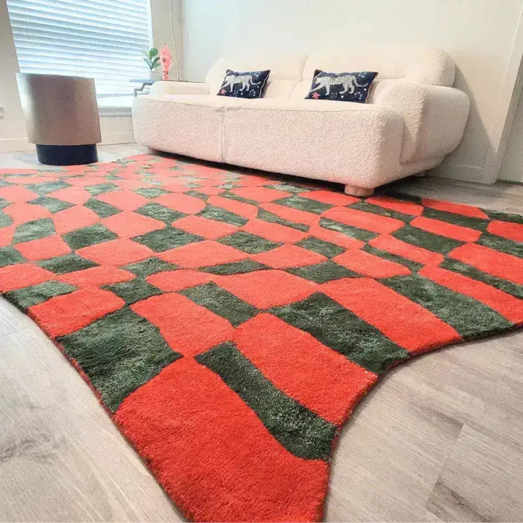 A vibrant Orange and Green Wavy Checker Hand Tufted Wool Rug adds a splash of color to a modern living room. The large area rug, perfect for living rooms, features an abstract design with wavy checker patterns, blending vintage charm with contemporary style. Ideal for use as kitchen rugs, hallway runner rugs, or bathroom runner rugs, this wool rug enhances any space with its bold colors and texture.