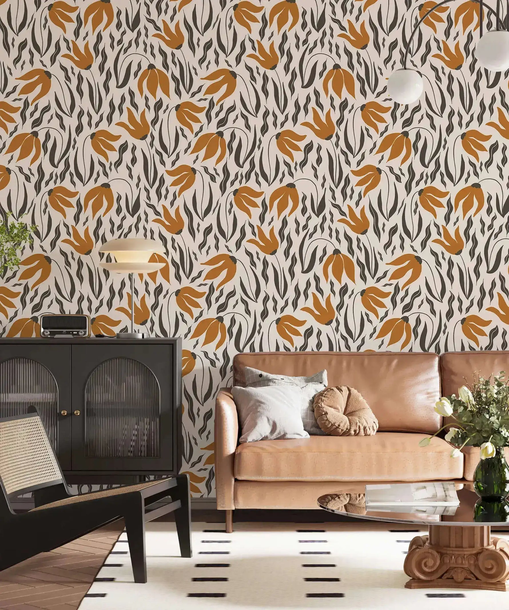 Orange Blossom Symphony Wallpaper of amber leaves and charcoal botanicals behind caramel sofa and dark ribbed cabinet.