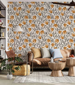 Orange Blossom Symphony Wallpaper with amber leaf and charcoal botanical motifs on cream behind a tan leather sofa.