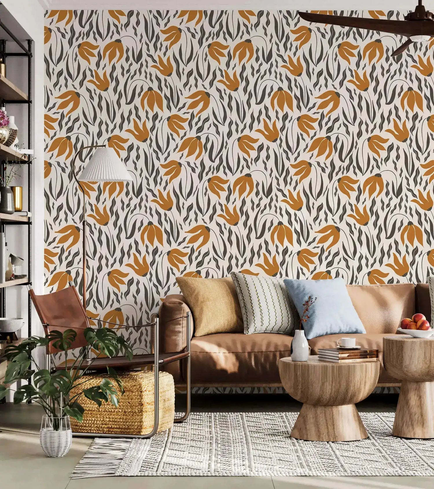 Orange Blossom Symphony Wallpaper with amber leaf and charcoal botanical motifs on cream behind a tan leather sofa.