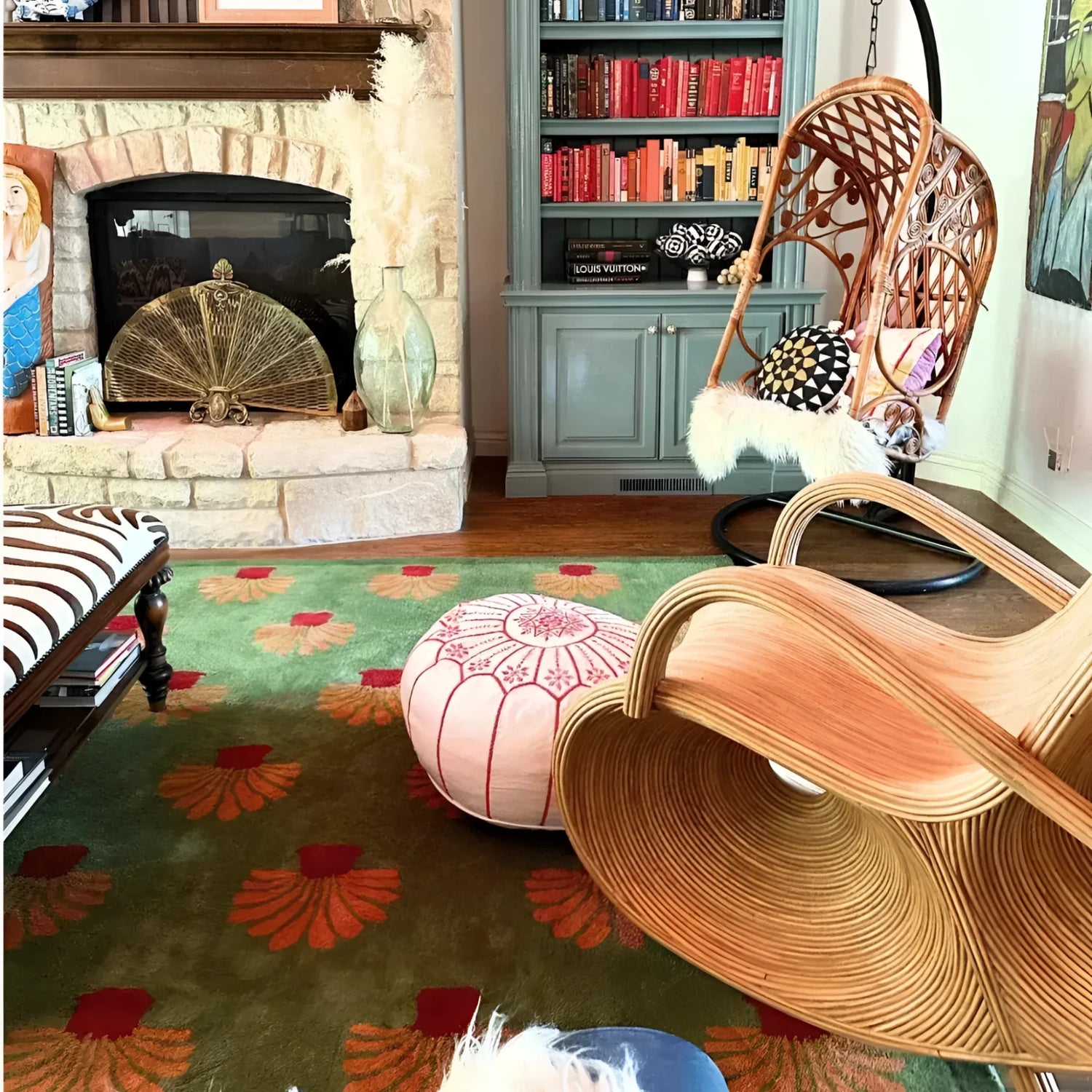 Cozy office space featuring a large area rug with vibrant orange palm tree patterns on a green tufted wool surface. The wool rug adds warmth and style to the room, complementing the eclectic decor with a hanging chair, pouf, and stone fireplace.