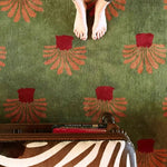 A vibrant large area rug with an abstract orange palm tree design on a lush green tufted wool surface, ideal for adding a splash of color to an office setting. The image shows a top view of the rug with bare feet standing on it, highlighting its cozy and inviting texture. Perfect for those seeking stylish wool rugs for office spaces.