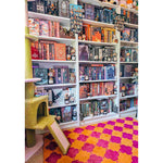 A vibrant Orange Pink Clovers Hand Tufted Area Rug placed in a cozy room, perfect for a living or dining room. The 8x10 wool rug adds a pop of color with its bold clover pattern, complementing the colorful bookshelves filled with various books and collectibles.