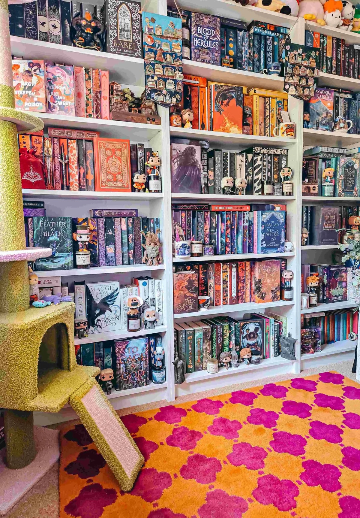 A vibrant Orange Pink Clovers Hand Tufted Area Rug placed in a cozy room, perfect for a living or dining room. The 8x10 wool rug adds a pop of color with its bold clover pattern, complementing the colorful bookshelves filled with various books and collectibles.