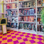 Bookshelf filled with books and figurines on a colorful floral-patterned rug.
