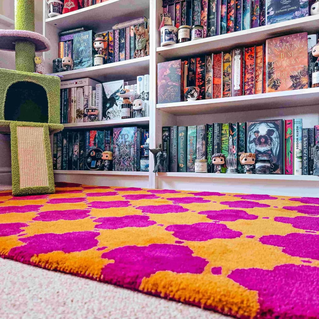 Bookshelf filled with books and figurines next to a colorful pink and yellow rug.