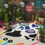 Colorful outdoor setting with a patterned rug, plants, and neon signs.