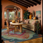 A stylish living room featuring the Orient Flame Hand Tufted Area Rug in an 8x10 size. The large wool rug showcases vibrant abstract patterns in rich colors, complementing the cozy decor of a living room or office setting. A wooden table, chairs, and a patterned sofa enhance the warmth of the space.