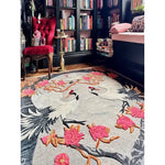 Oriental Reverie Hand Tufted Area Rug in a cozy bedroom setting, featuring an elegant floral design with cranes and vibrant pink flowers. This wool rug adds a touch of sophistication and warmth to the room, complementing the rich red chair and well-stocked bookshelves. Perfect for enhancing any bedroom or living room space.