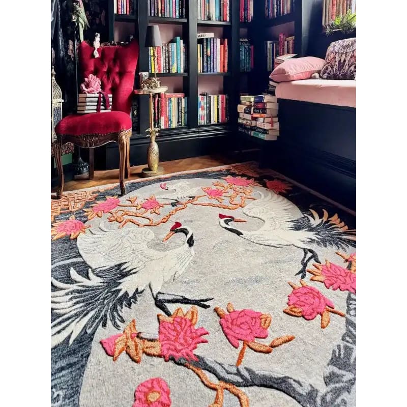 Oriental Reverie Hand Tufted Area Rug in a cozy bedroom setting, featuring an elegant floral design with cranes and vibrant pink flowers. This wool rug adds a touch of sophistication and warmth to the room, complementing the rich red chair and well-stocked bookshelves. Perfect for enhancing any bedroom or living room space.