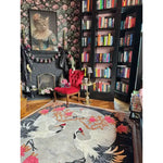 A beautifully designed area rug featuring an elegant floral pattern with cranes, perfect for adding a touch of sophistication to your bedroom or living room. This wool rug enhances the cozy ambiance of the room, complementing the vibrant red chair and the stylish bookshelf filled with colorful books.
