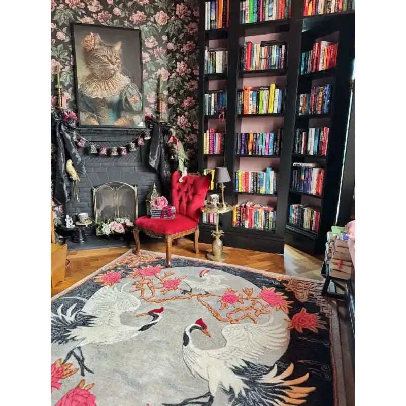 A beautifully designed area rug featuring an elegant floral pattern with cranes, perfect for adding a touch of sophistication to your bedroom or living room. This wool rug enhances the cozy ambiance of the room, complementing the vibrant red chair and the stylish bookshelf filled with colorful books.