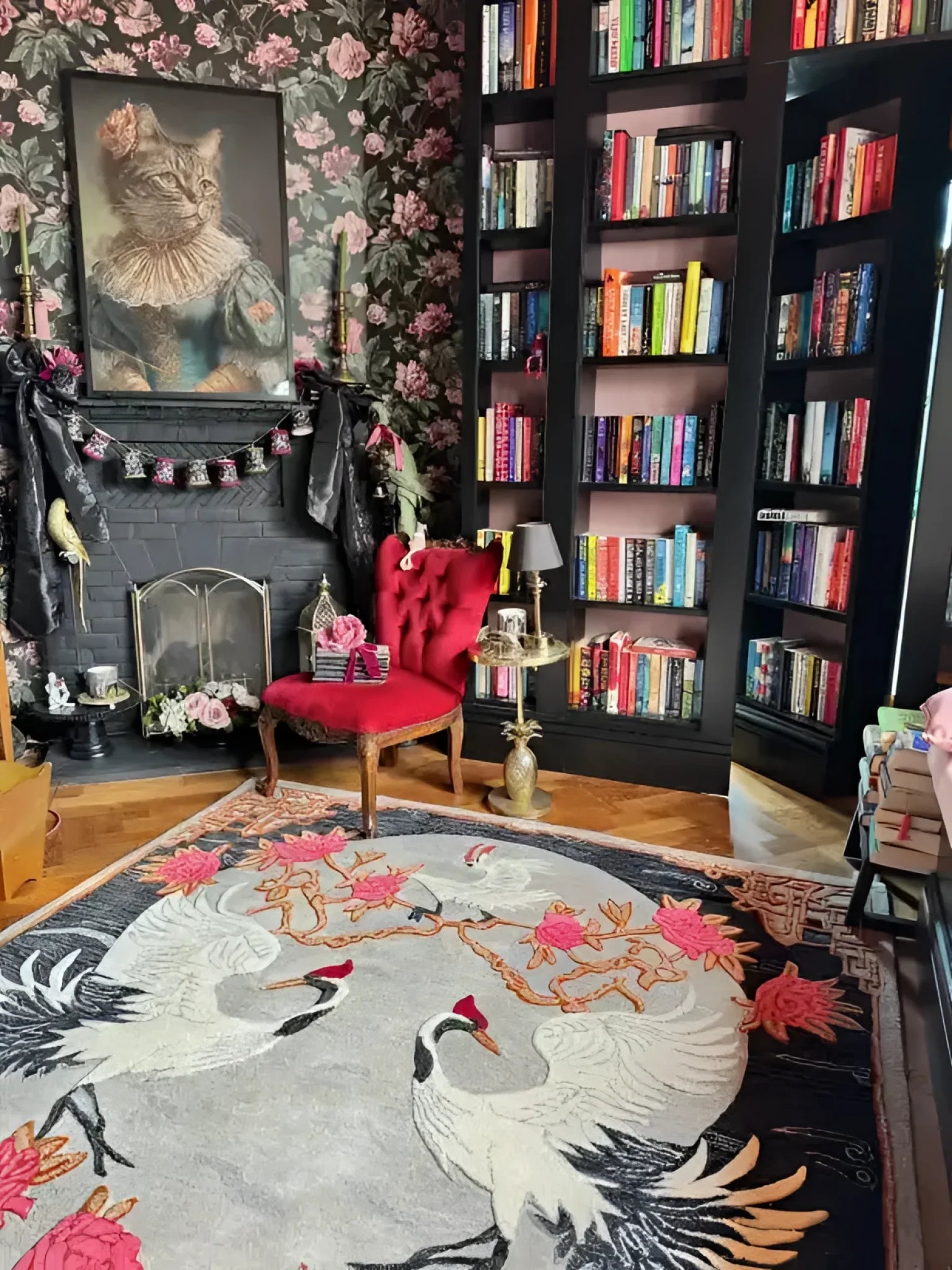 A beautifully designed area rug featuring an elegant floral pattern with cranes, perfect for adding a touch of sophistication to your bedroom or living room. This wool rug enhances the cozy ambiance of the room, complementing the vibrant red chair and the stylish bookshelf filled with colorful books.