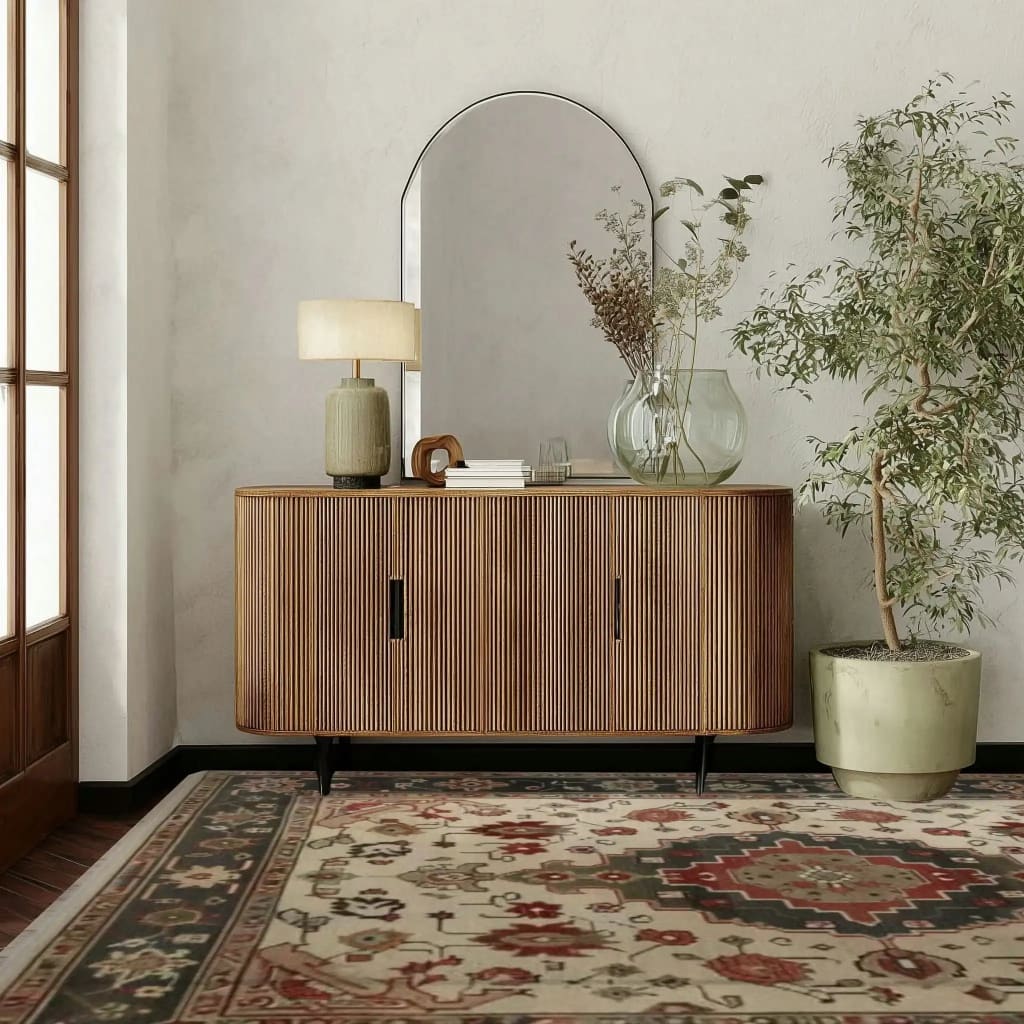 Wooden sideboard with decorative items, persian rug, in a room with a large mirror, lamp, and plant.