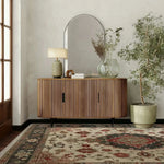 Wooden sideboard with decorative items, persian rug, in a room with a large mirror, lamp, and plant.
